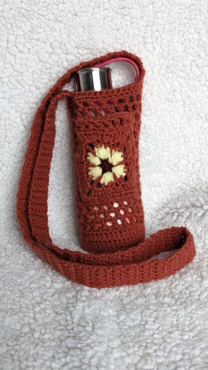 Orange mesh crochet water bottle holder with a yellow flower pocket in the front.